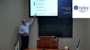 Speaker pointing to a timeline slide showing dates of historical additions to church practice