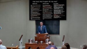 Speaker at the pulpit teaching on the kingdom and Christ's church, with a slide showing Isaiah 2, Daniel 2, and Joel 2